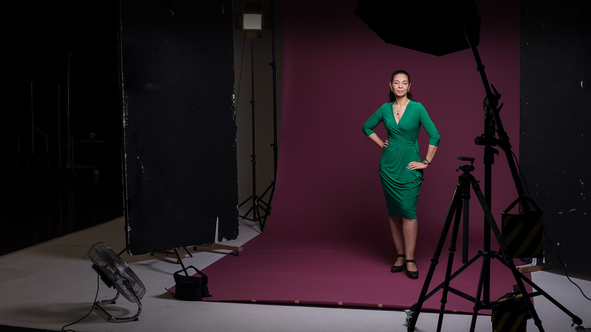 Woman in a green dress on a photoshoot set in front of a maroon backdrop