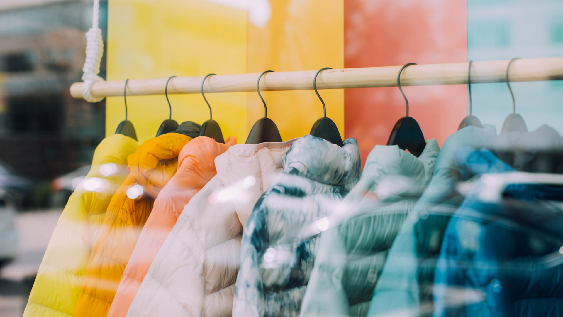 Photograph of jackets of various colours hanging on a rail inside shop window